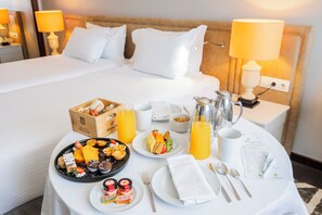 A neatly made breakfast table with a variety of pastries, fruits, and beverages, set in a hotel room with a large bed and bedside lamps. - Holiday Inn Porto Gaia by IHG (Vila Nova de Gaia)