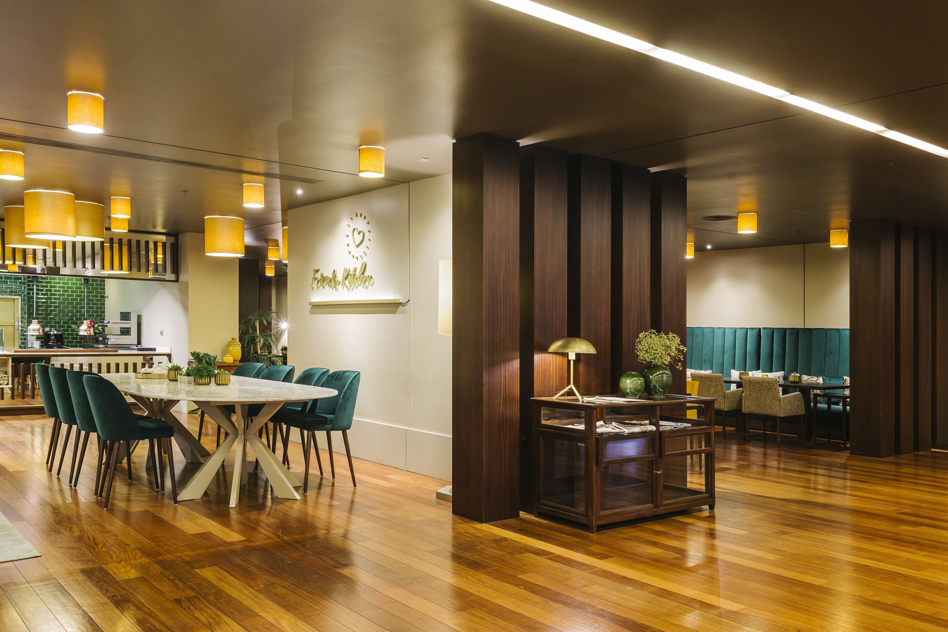 Un comedor amplio con piso de madera, una mesa redonda y sillas color turquesa. Se ve una zona de cocina con un salpicadero verde al fondo.