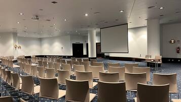 A conference room with rows of chairs, a large screen, and a projector.