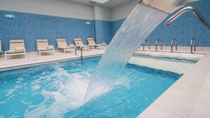Una piscina con fuente, sillones de descanso y pared de azulejos azules.