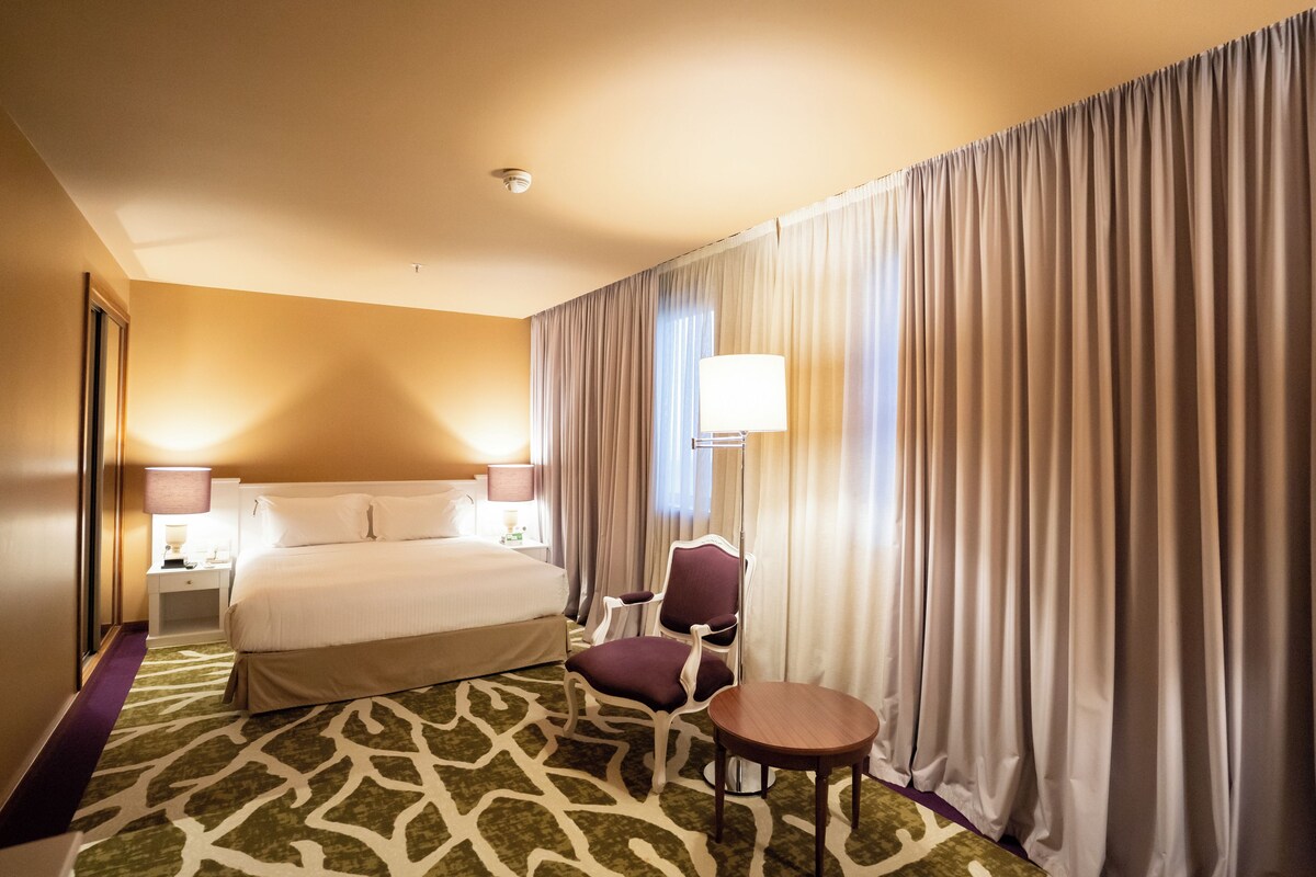 Een hotelkamer met een groot bed, een stoel, een tafeltje en een lamp.