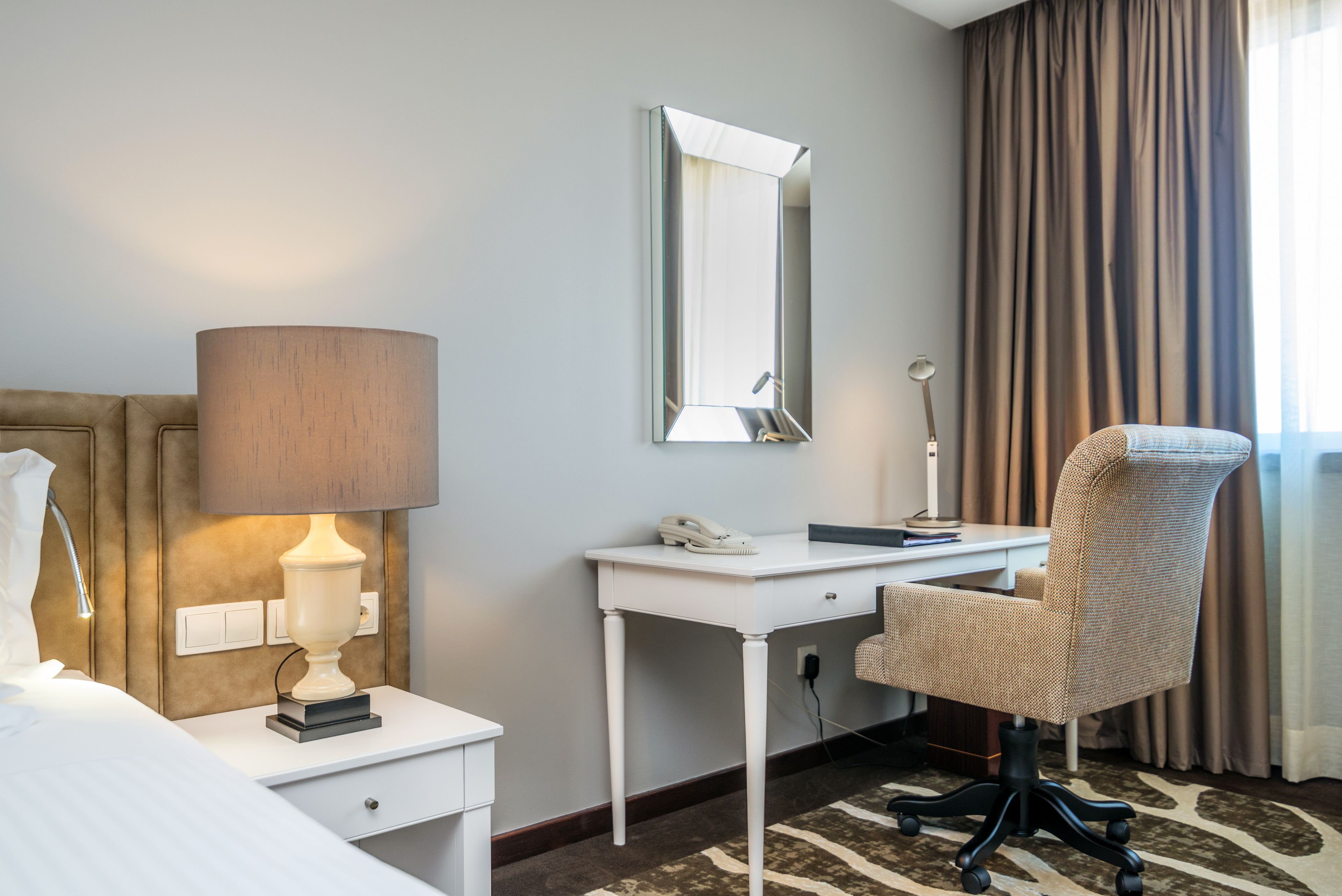 Une chambre d’hôtel équipée d’un lit, d’une lampe de chevet, d’un bureau, d’une chaise et d’un grand miroir.