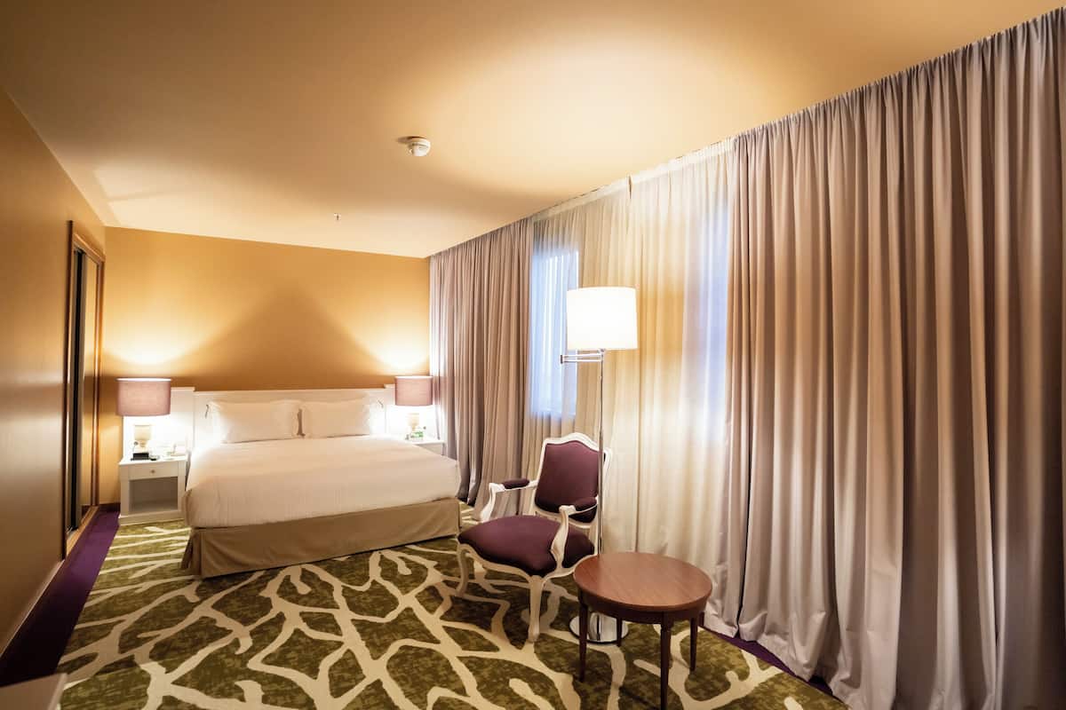 Une chambre d’hôtel avec un grand lit, une chaise, une petite table et une lampe.