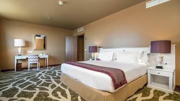 A hotel room with a large bed, a desk, a chair, and two bedside lamps.