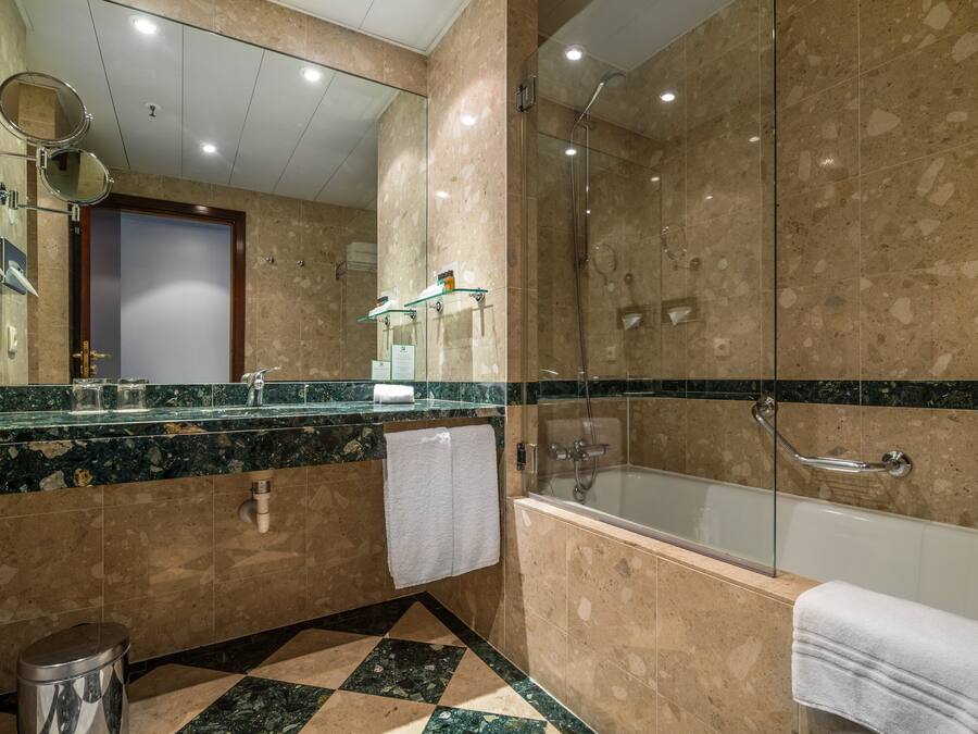 A modern bathroom with a glass-enclosed shower, a large mirror, and a marble-tiled floor.