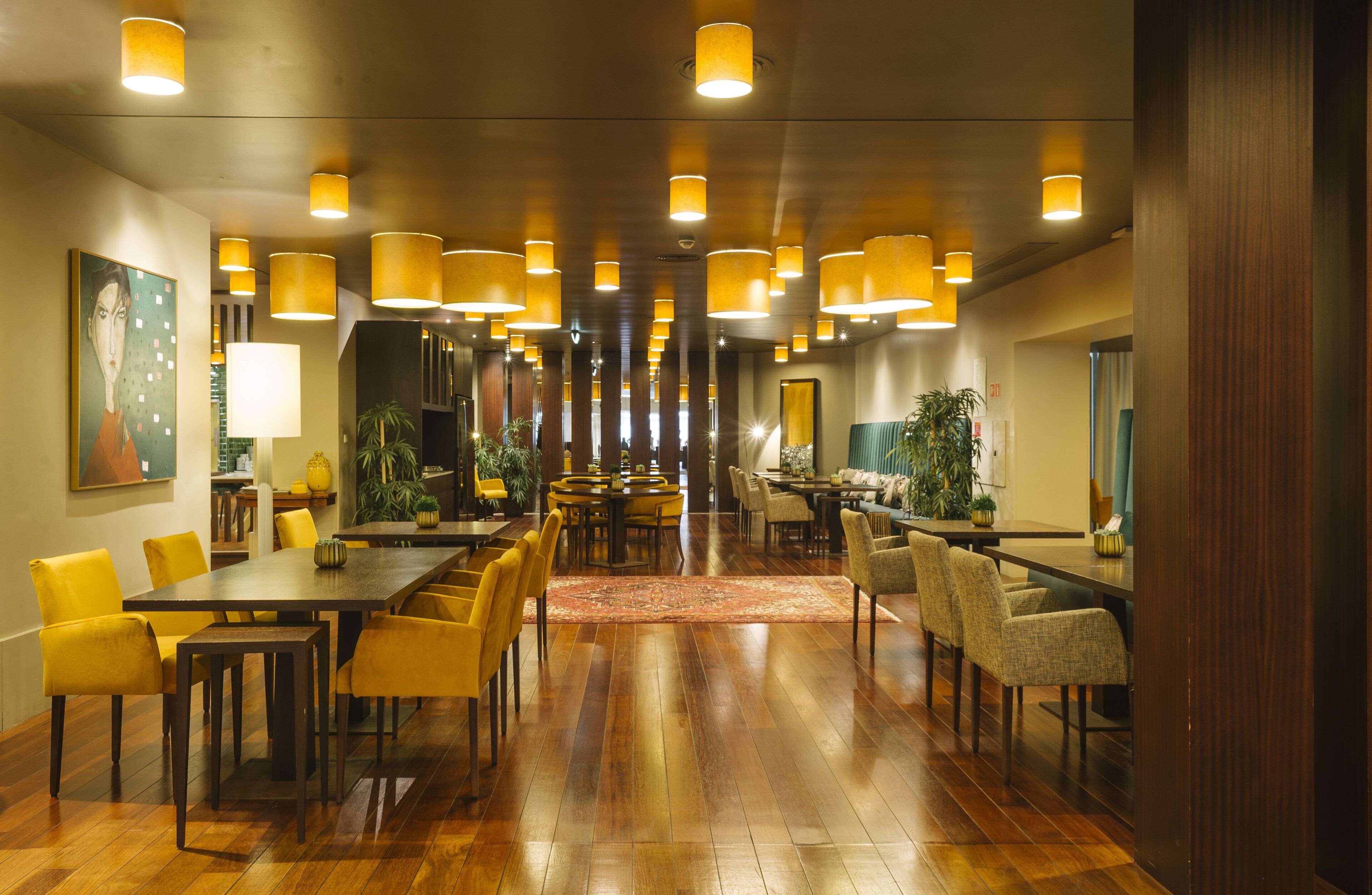 Un comedor amplio con varias mesas y sillas, iluminación cálida y plantas decorativas.