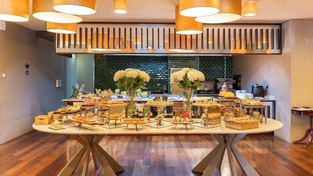 Una mesa de buffet con diferentes alimentos y flores, ubicada en un salón con piso de madera e iluminación moderna.