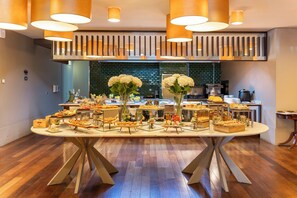 A buffet table with various food items and flowers, set in a room with wooden flooring and modern lighting fixtures. - Holiday Inn Porto Gaia by IHG (Vila Nova de Gaia)