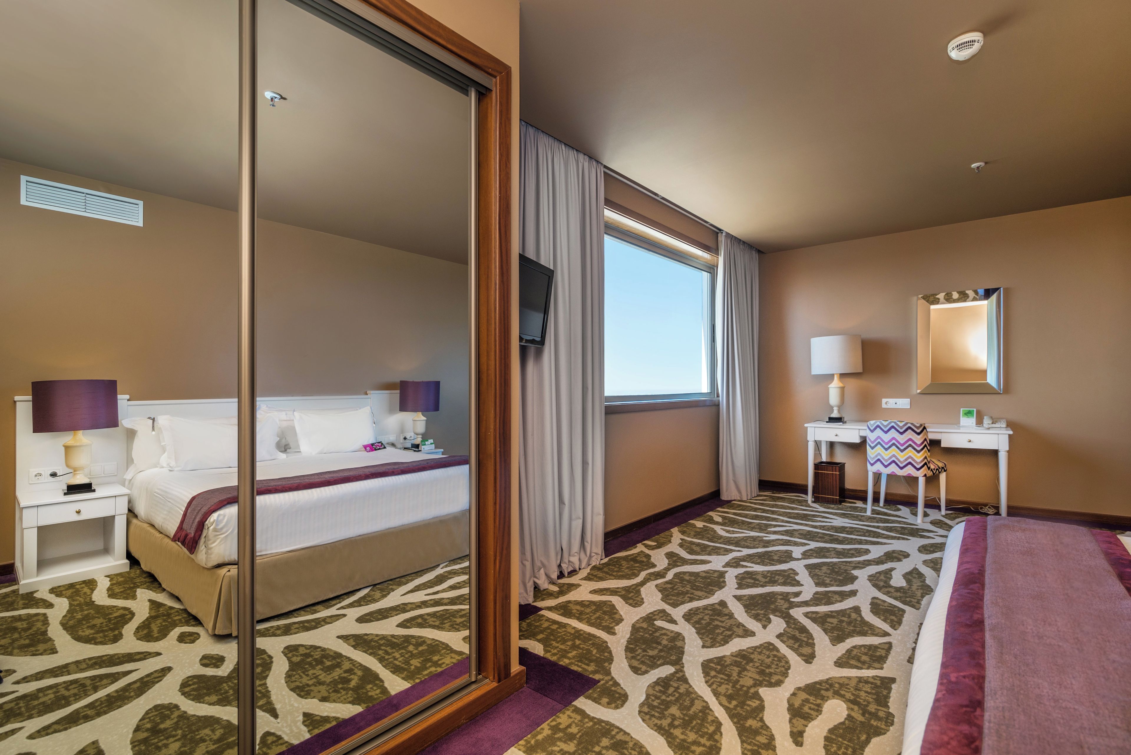 A hotel room with a bed, a desk, a chair, a television, and a window with curtains.