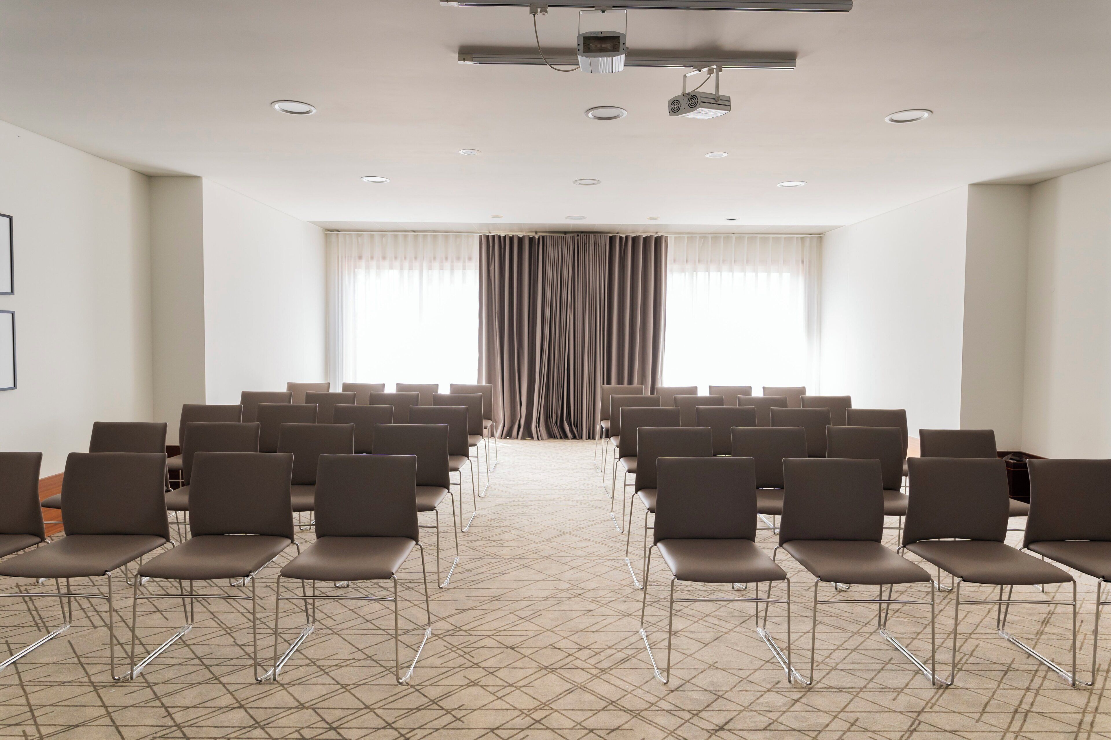 Un salón de conferencias con filas de sillas, un proyector y un amplio ventanal con cortinas.
