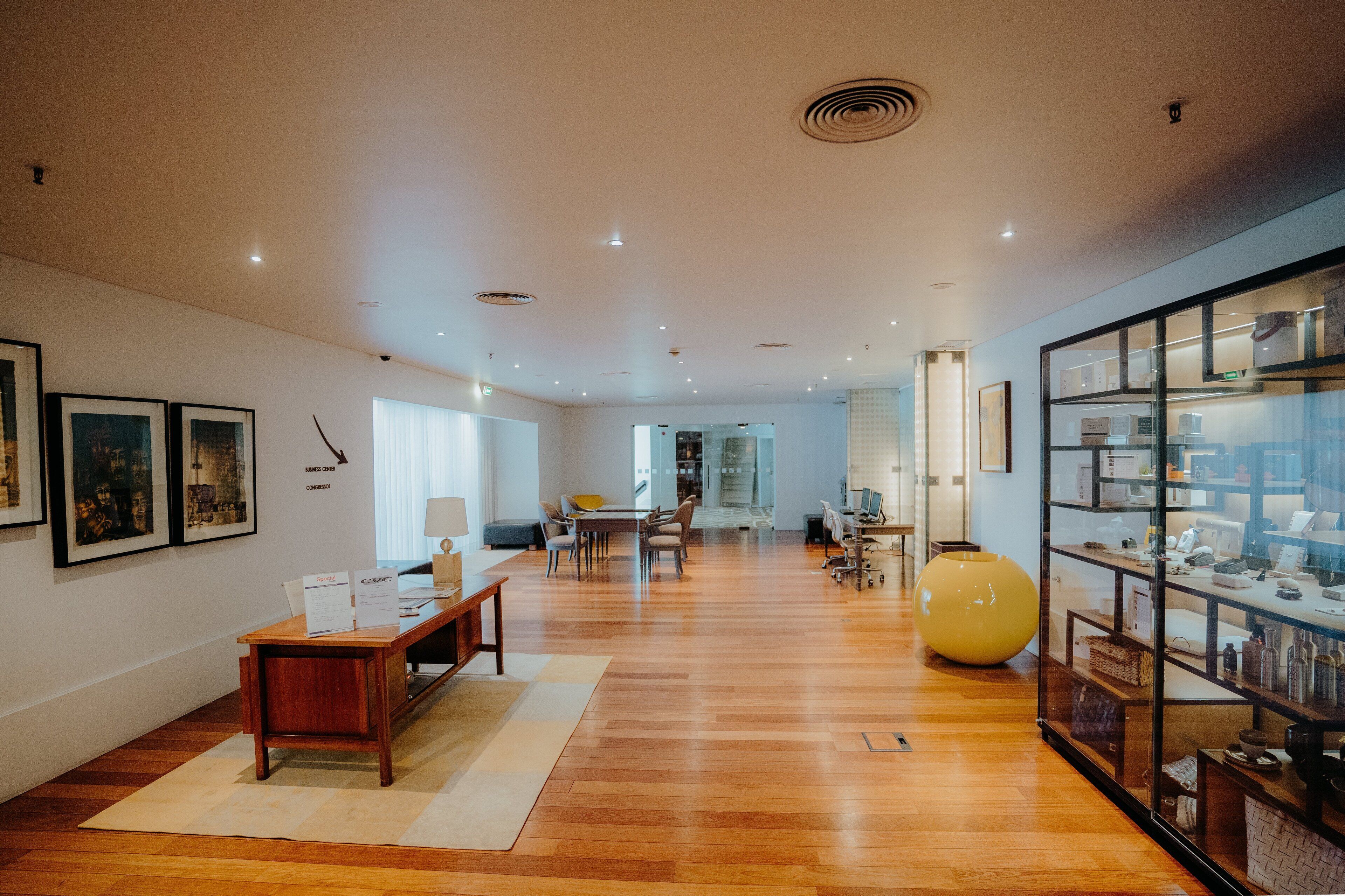 A spacious living area with wooden flooring, a central seating arrangement, a large vase, and a glass display cabinet.