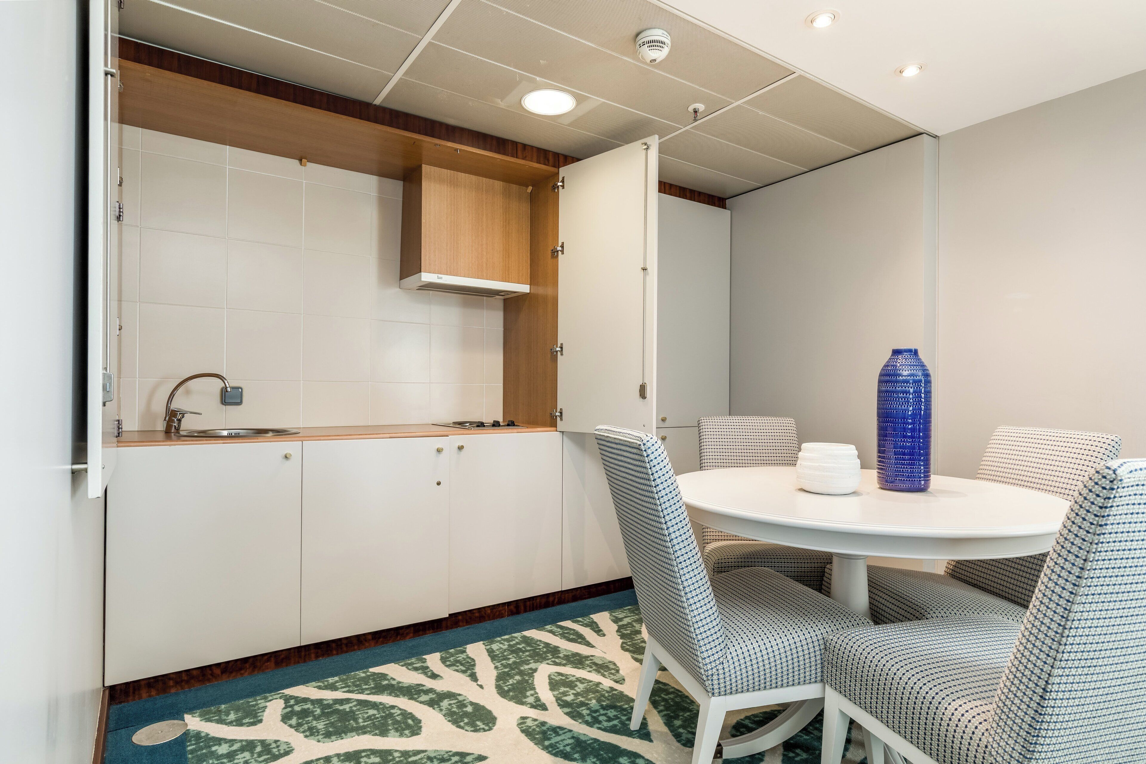 A modern kitchen with white cabinets, a wooden countertop, and a round dining table with patterned chairs.