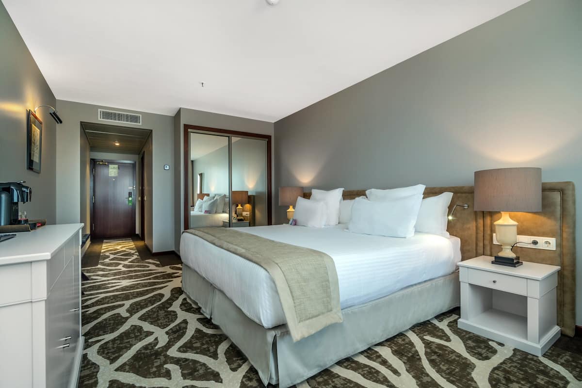 Une chambre d’hôtel avec un grand lit, des tables de chevet, une armoire et un miroir.
