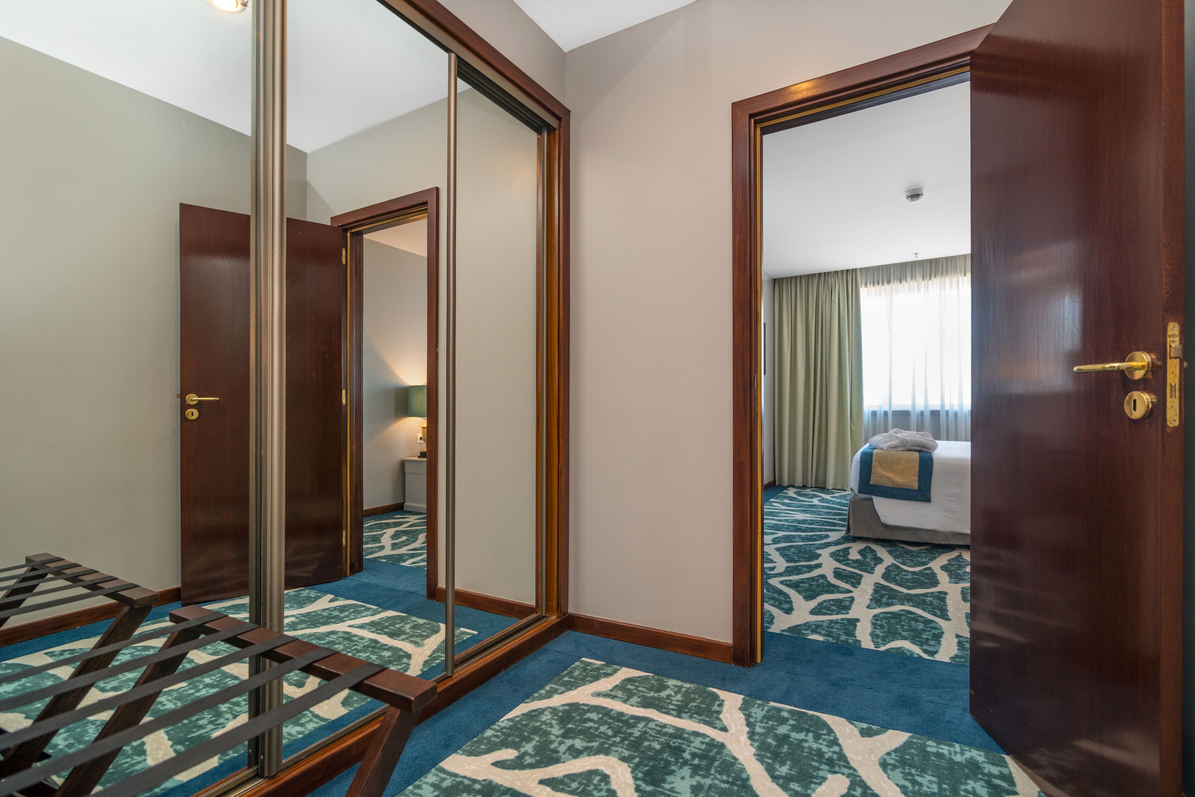 Una habitación de hotel con un espejo grande, una cama con colcha de rayas azules y blancas, y piso de madera.