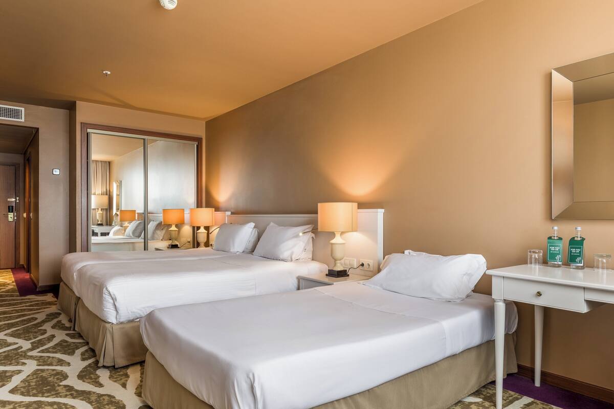 Une chambre d’hôtel avec deux lits, un bureau, un miroir et deux lampes.