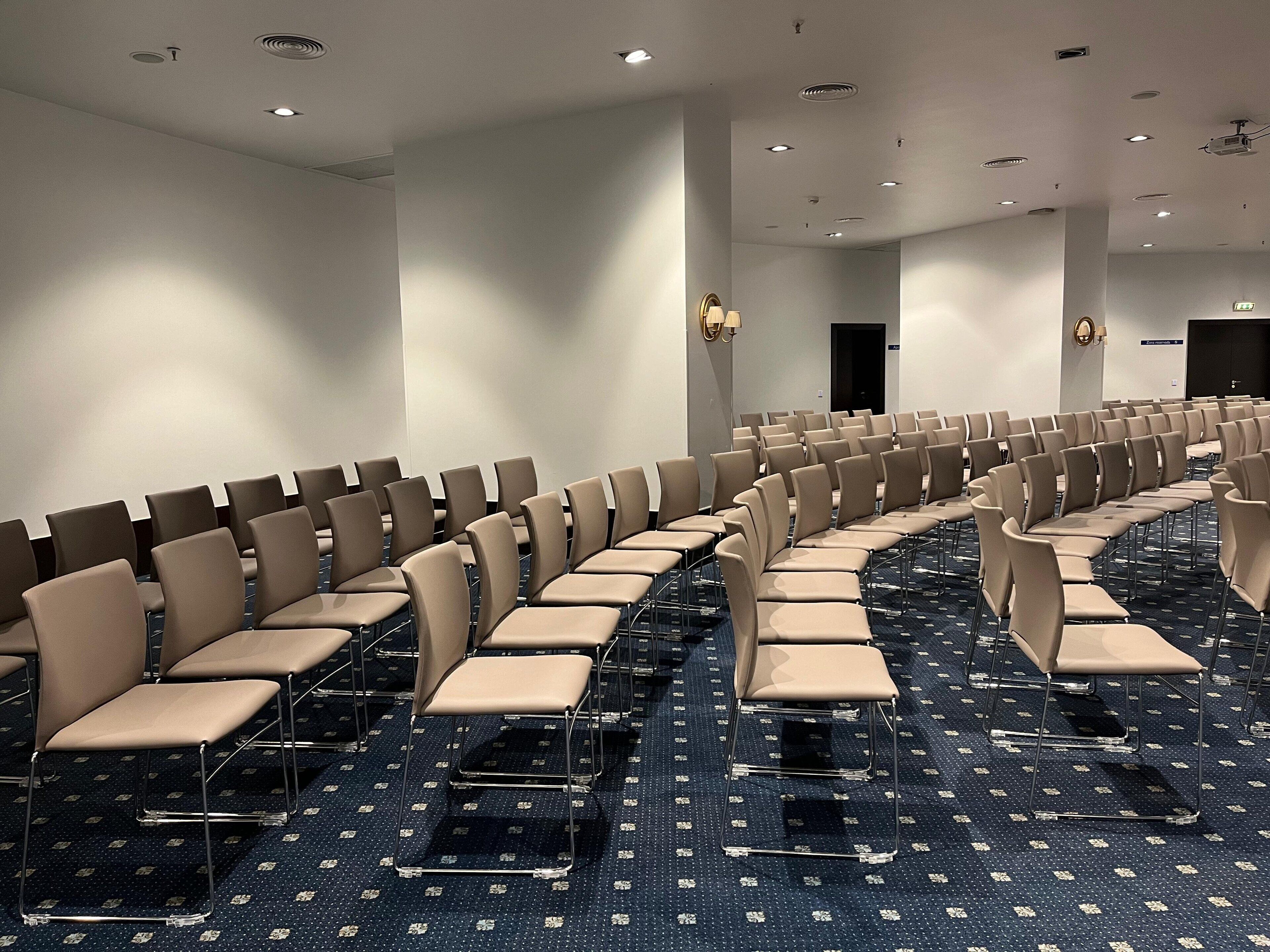 A conference room with rows of beige chairs and a patterned carpet.
