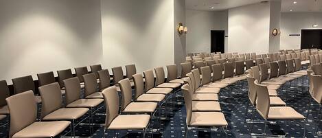 A conference room with rows of beige chairs and a patterned carpet.