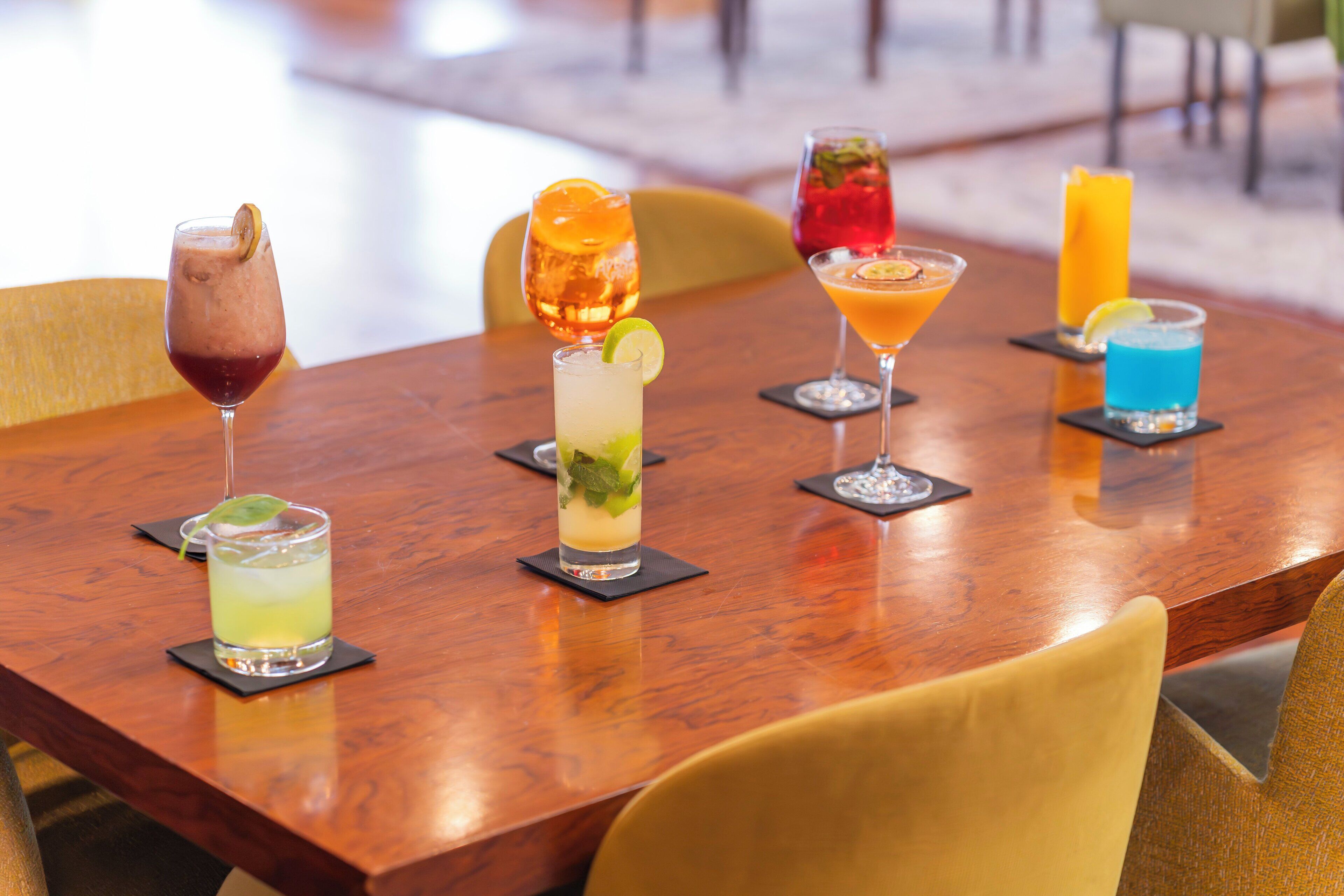 Een houten tafel met zes verschillende cocktails, elk gegarneerd met een partje lime.