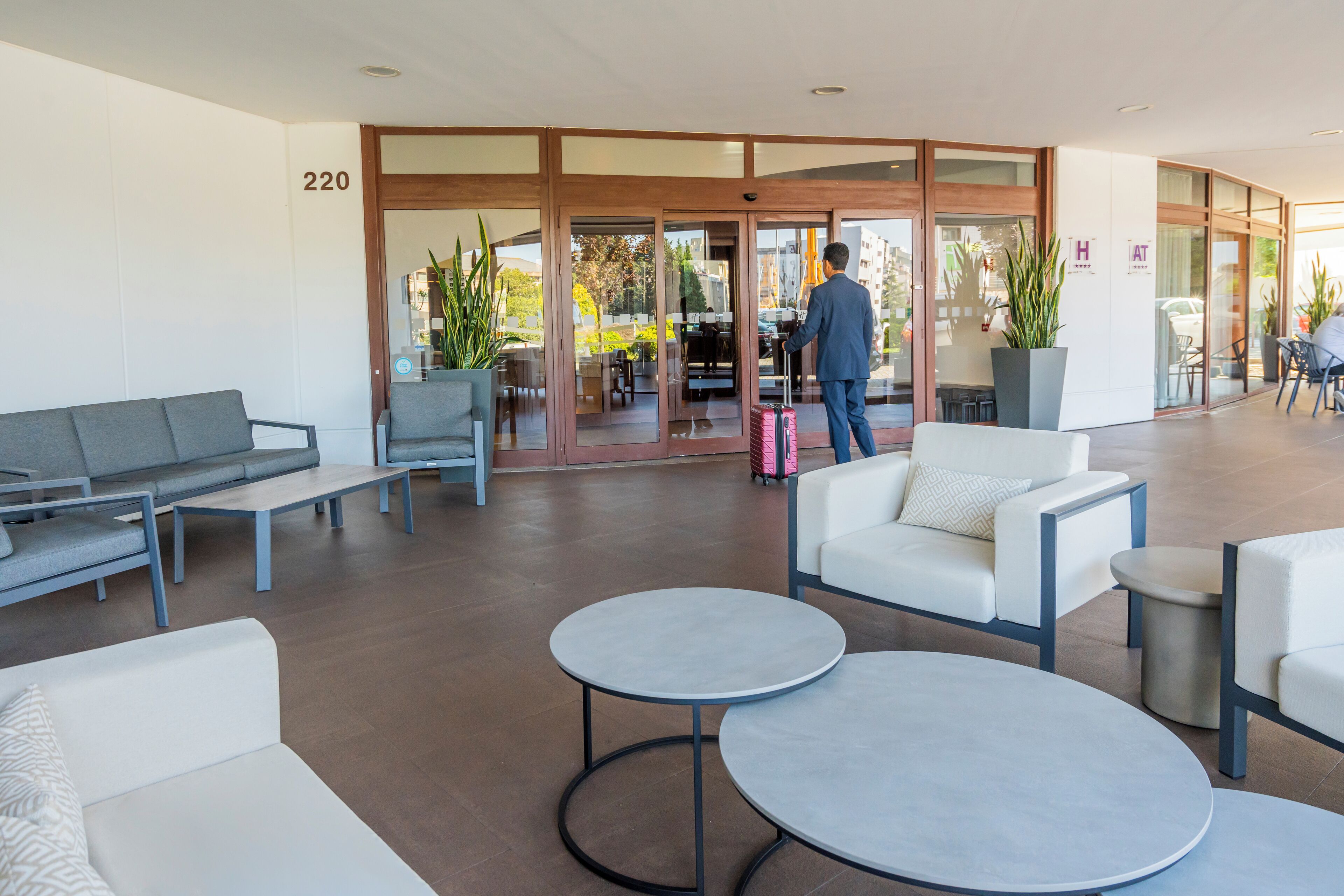 Un moderno vestíbulo de hotel con una zona de estar, un mostrador de recepción y una entrada por puerta de cristal.