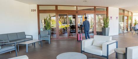 A modern hotel lobby with a seating area, a reception desk, and a glass door entrance.
