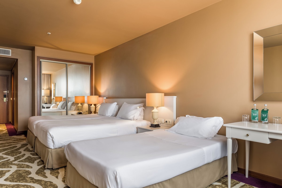 Een hotelkamer met twee bedden, een bureau, een spiegel en twee lampen.