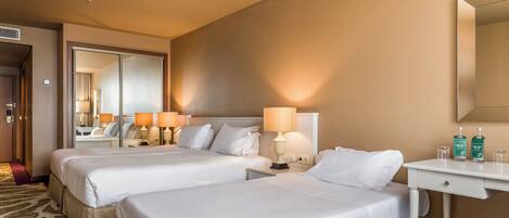 A hotel room with two beds, a desk, a mirror, and two lamps.
