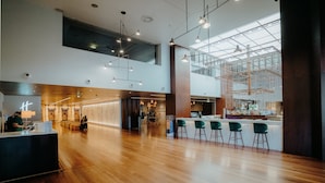 Un vestíbulo amplio con suelo de madera, un mostrador de recepción y una zona de bar con sillas verdes.