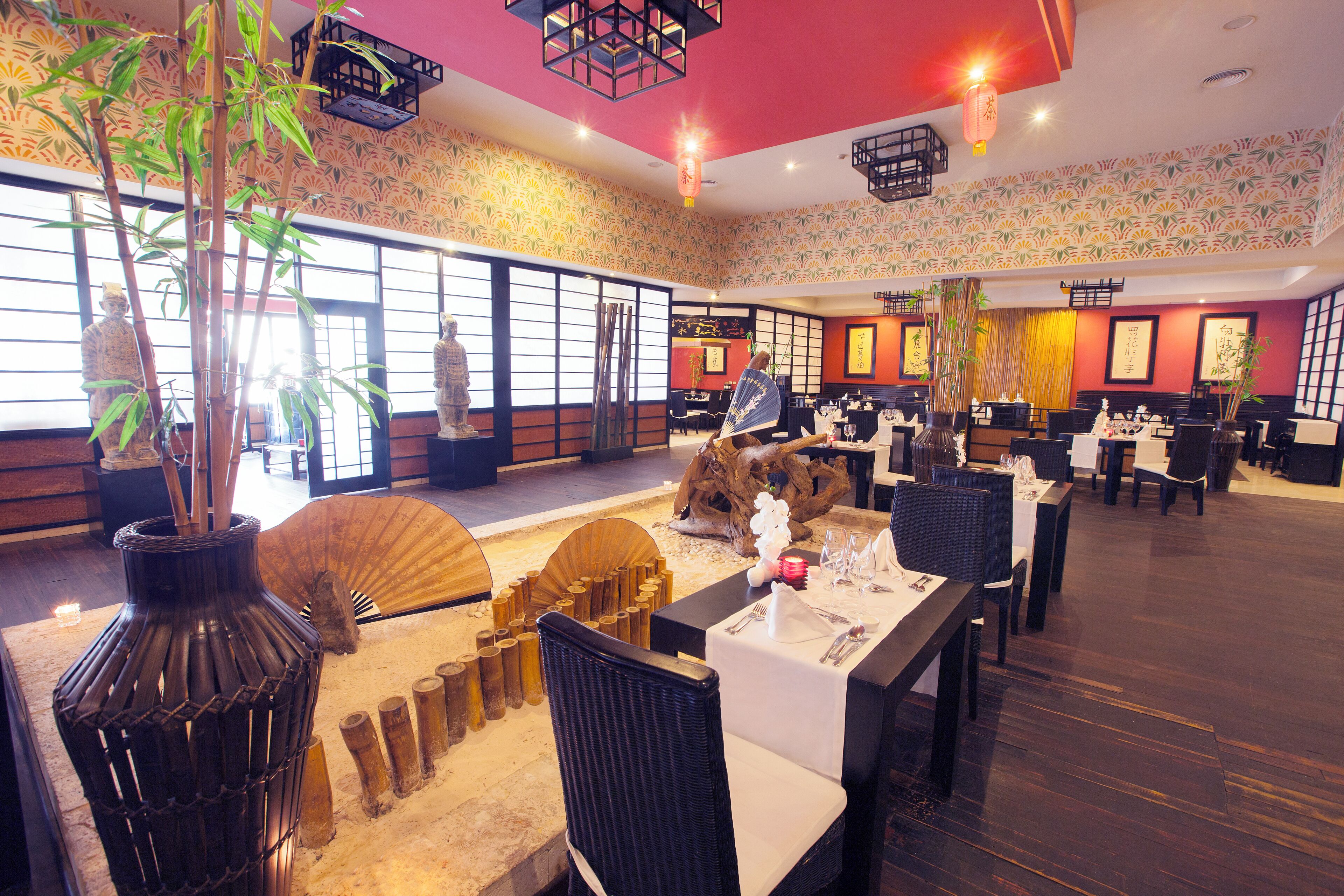 Ein Restaurant mit traditioneller Einrichtung, darunter Bambuspflanzen und ein Ventilator. Die Tische sind mit weißen Tischdecken und Geschirr gedeckt.