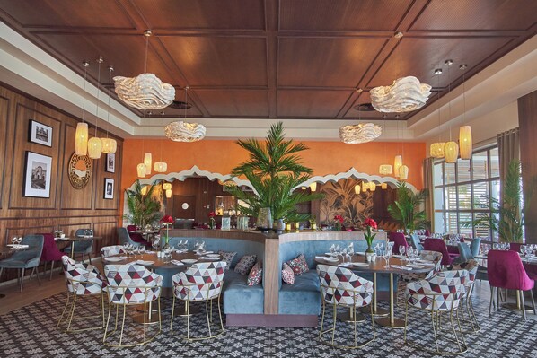 A restaurant with a central bar, patterned chairs, and a tropical plant centerpiece.