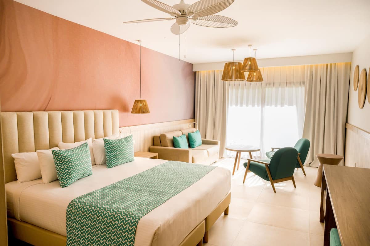 Una habitación de hotel con una cama grande, un sofá, una mesa de comedor y un ventilador de techo.