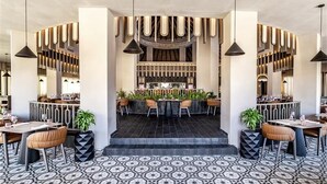 Ein modernes Restaurantambiente mit einer zentralen Bar, hohen Decken und einem gemusterten Boden.