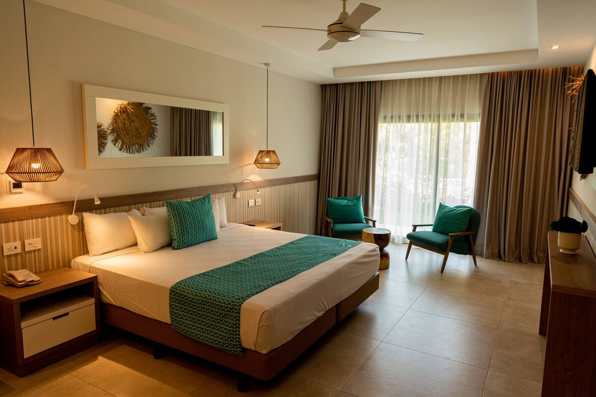 Una habitación de hotel con una cama grande, un ventilador de techo, un escritorio, una silla y una ventana con cortinas.
