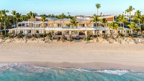 Un hotel sulla spiaggia con diversi edifici, una spiaggia sabbiosa e palme.
