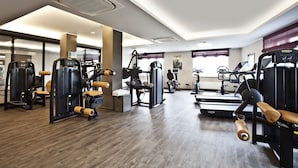 Une salle de sport moderne équipée de divers appareils d’exercice, d’un tapis de course et d’un miroir.