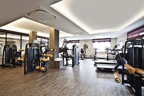 Une salle de sport moderne équipée de divers appareils d’exercice, d’un tapis de course et d’un miroir.