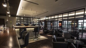 Un espace bar moderne doté d’un long comptoir, de tabourets et d’un coin salon avec des tables et des chaises.