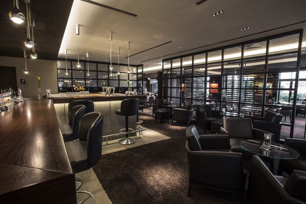 Een moderne bar met een lange toonbank, barkrukken en een zithoek met tafels en stoelen.