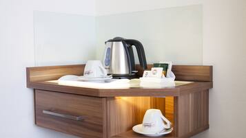 Una kitchenette en esquina con cafetera, hervidor de agua y una taza de café.