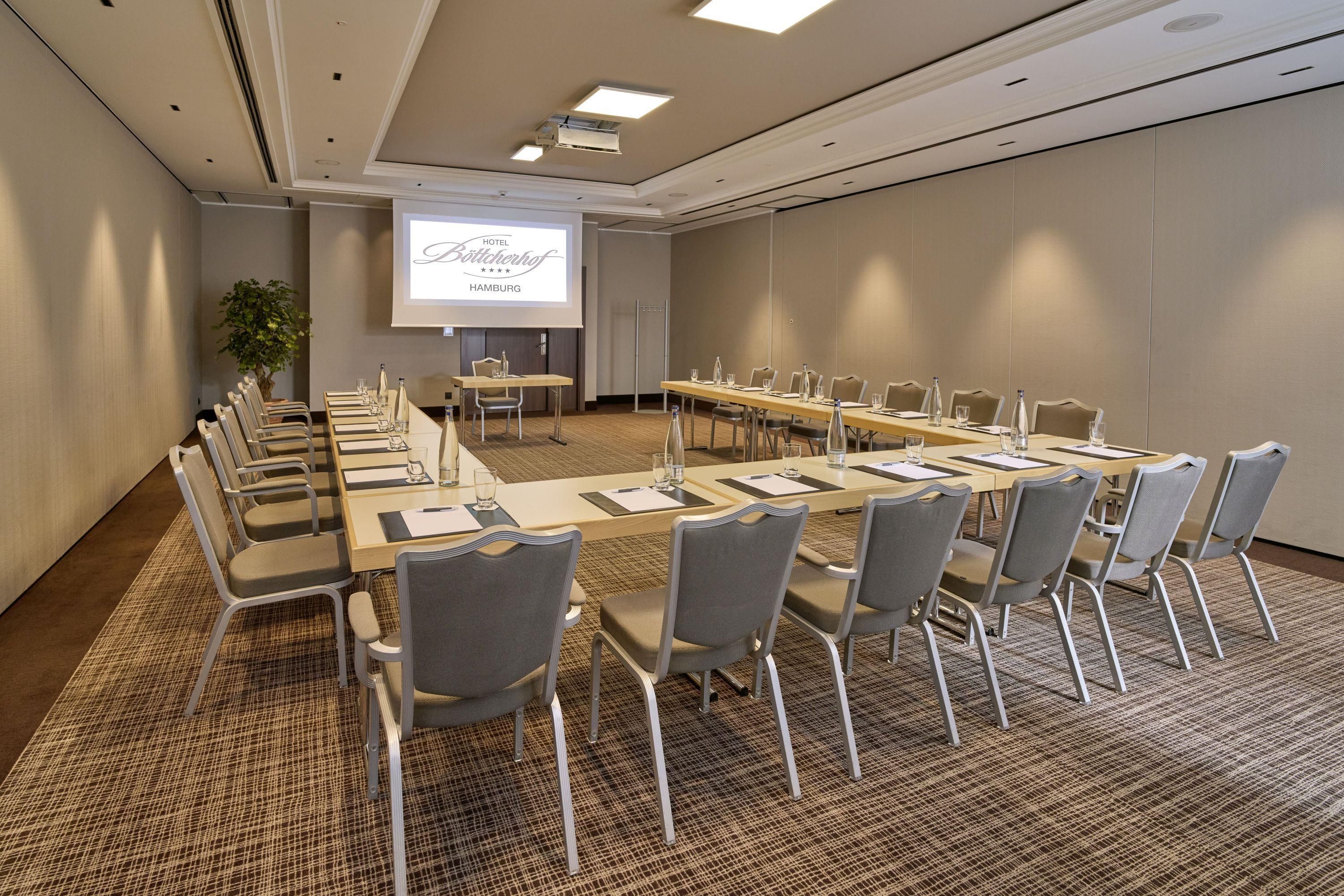 A conference room with a long table, chairs, a projector screen, and a plant.