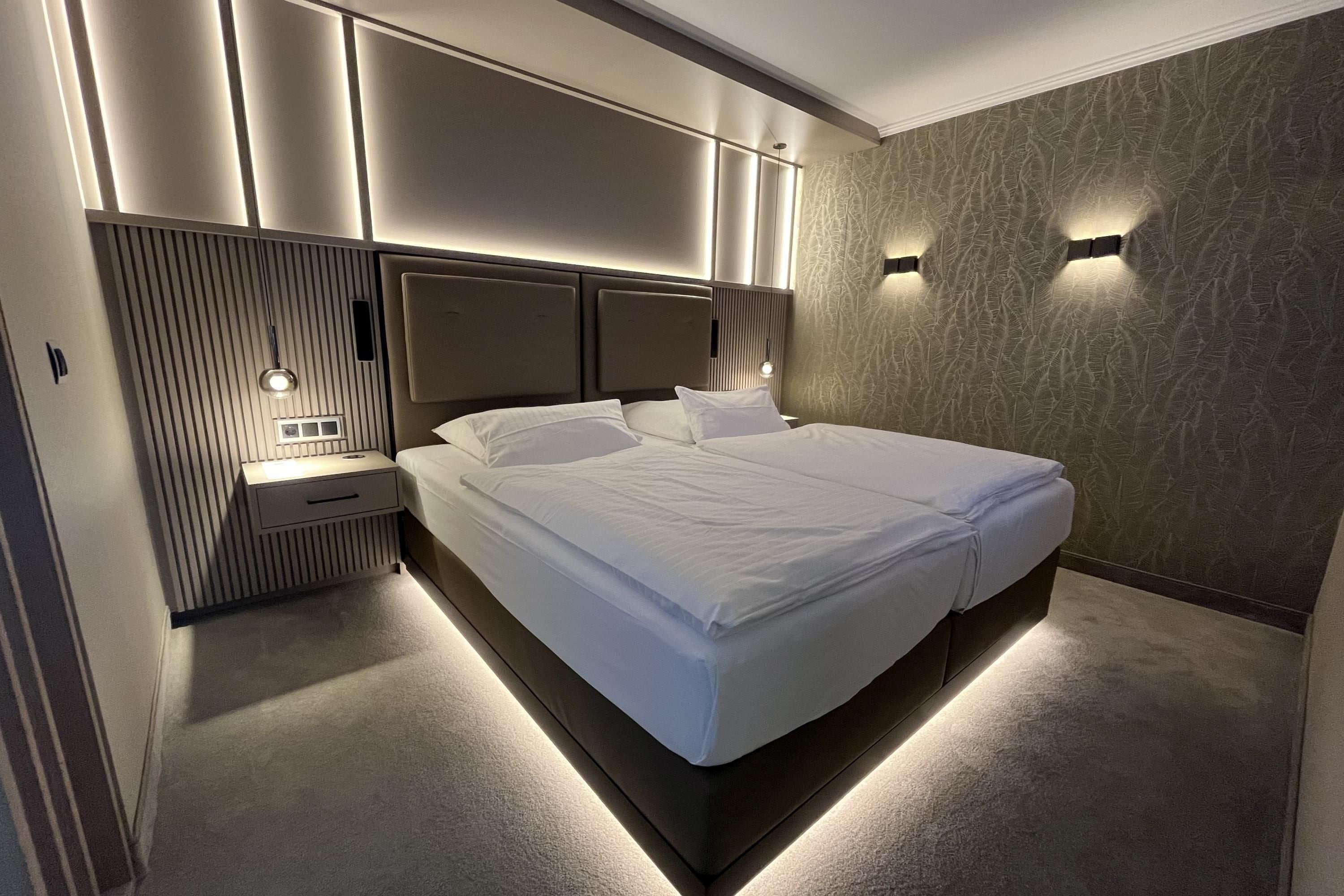 Quarto moderno com cama grande, mesas de cabeceira e iluminação embutida na parede.