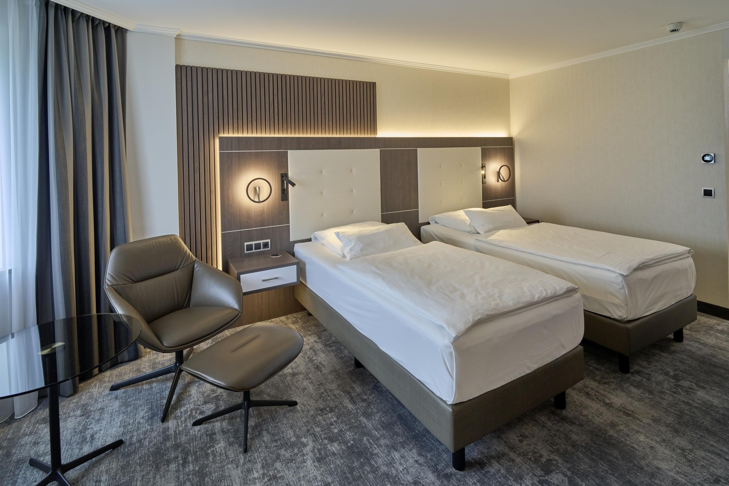 A hotel room with two beds, a desk, a chair, and a large mirror.