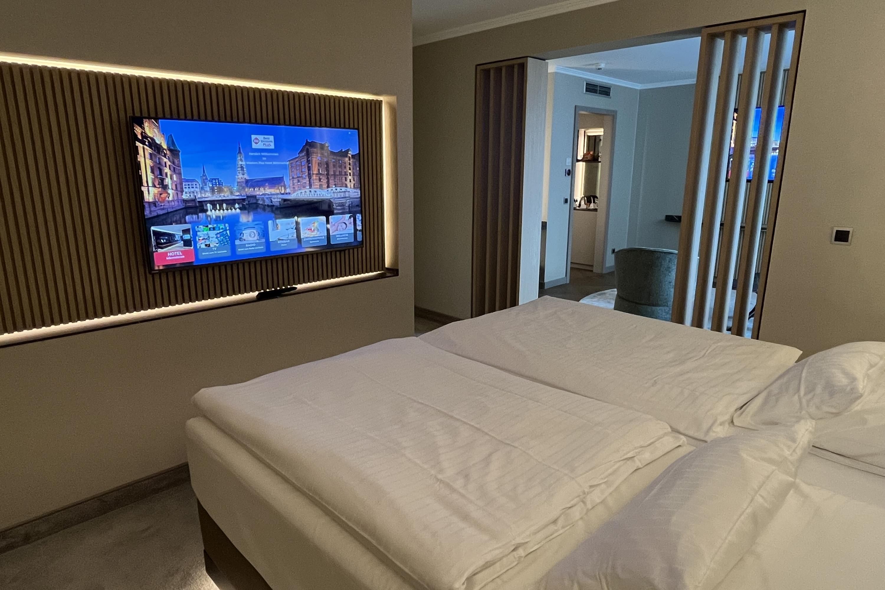 A hotel room with a bed, a television mounted on the wall, and a view of the hallway.
