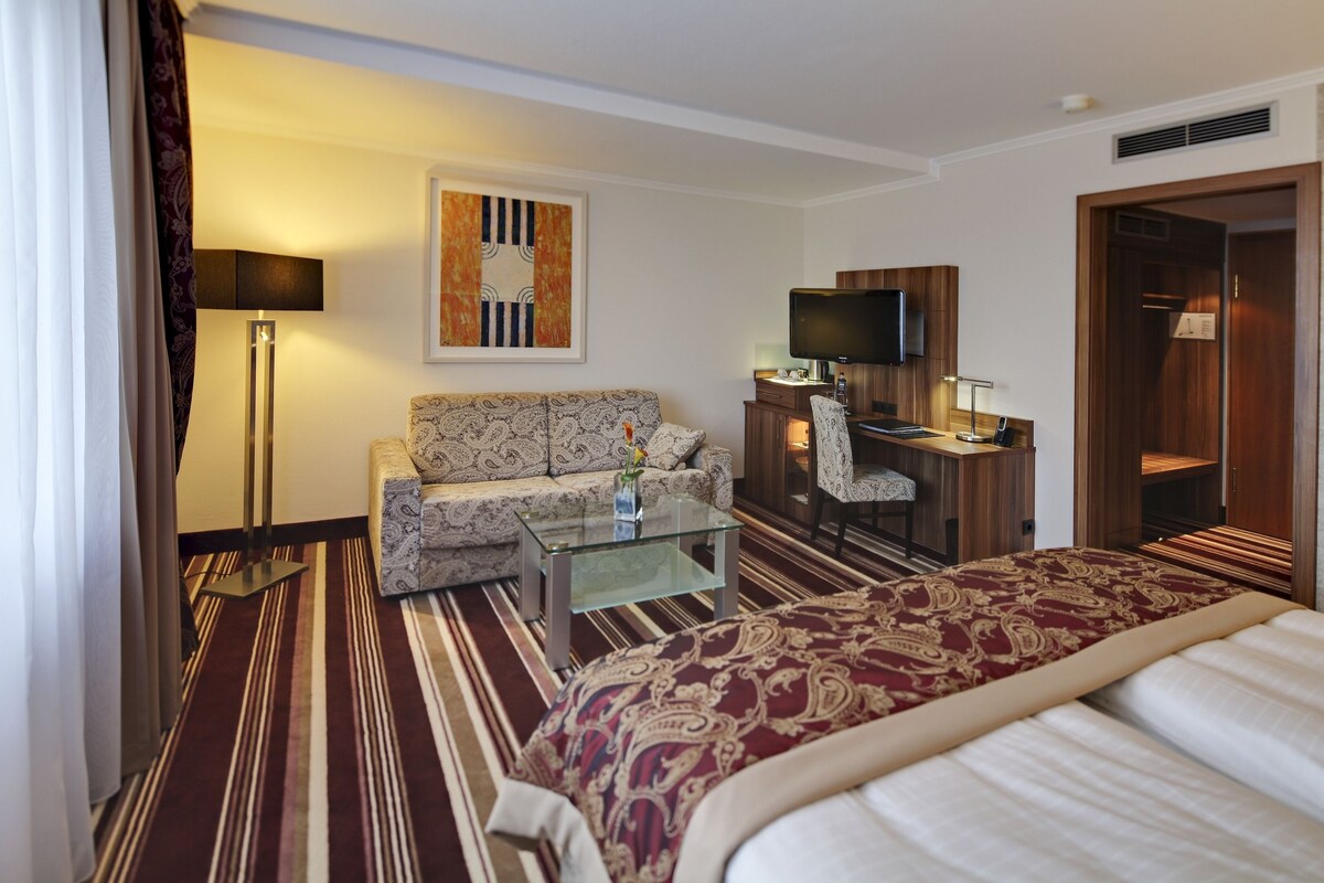 Une chambre d’hôtel équipée d’un lit, d’un canapé, d’un bureau avec un ordinateur, d’une télévision et d’une lampe.
