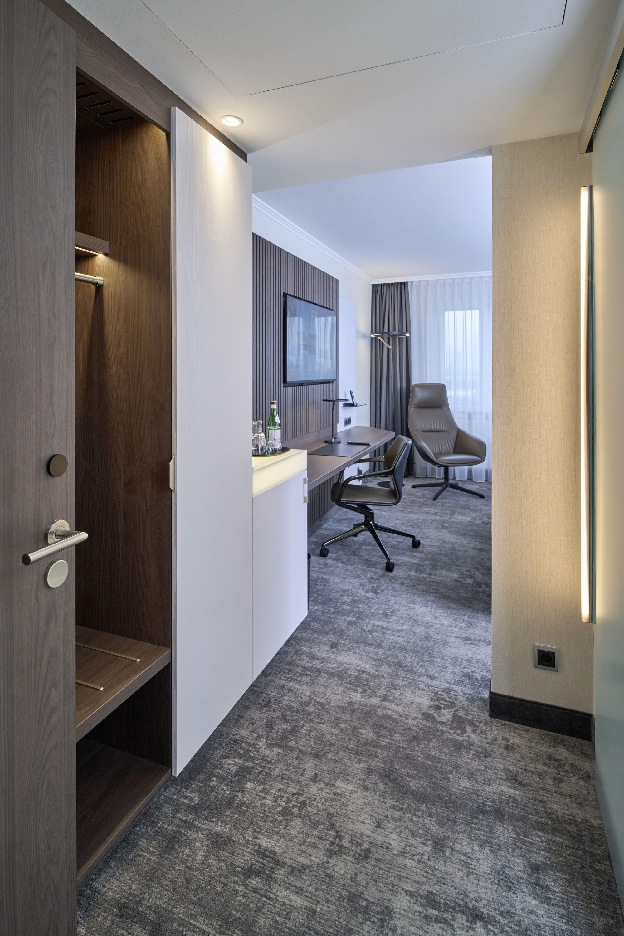 A hotel room with a desk, chair, and a television mounted on the wall.