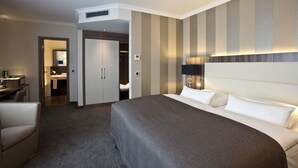 Une chambre d’hôtel avec un grand lit, un bureau, une chaise, une armoire et une salle de bain visible à travers une porte ouverte.