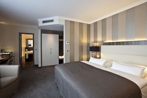 Hotelkamer met een groot bed, een bureau, een stoel, een kledingkast en een badkamer die door een geopende deur zichtbaar is.