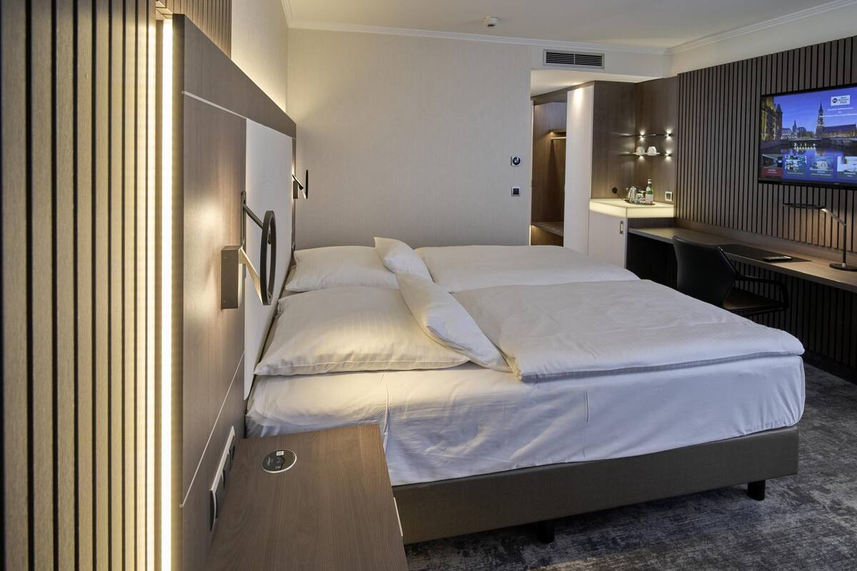 Quarto de hotel moderno com uma cama grande, uma escrivaninha e uma televisão.