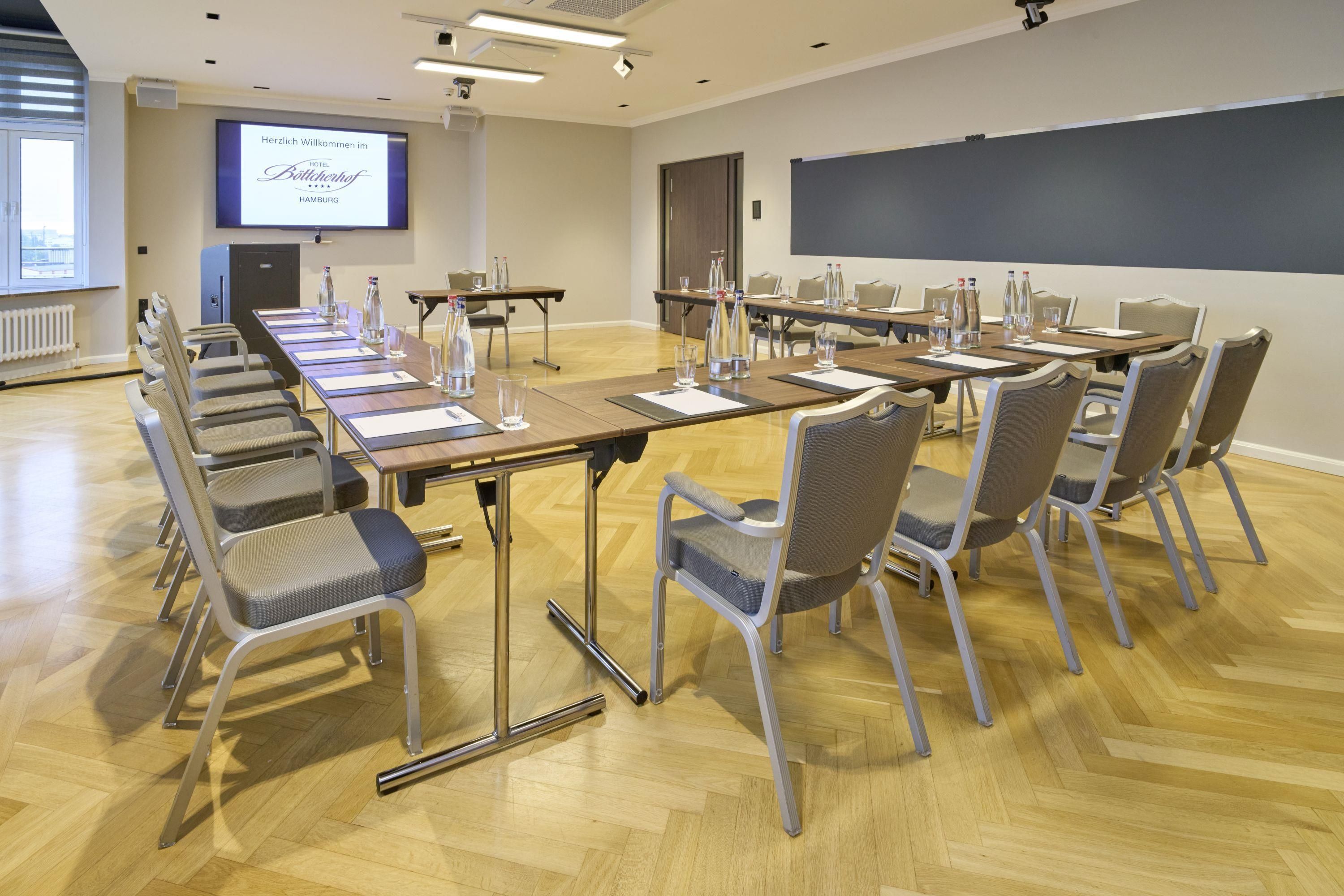 Ein Konferenzraum mit einem langen Tisch, Stühlen und einer Projektionsleinwand.