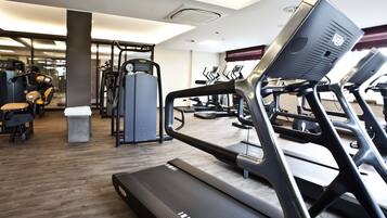 Et fitnessrum med løbebånd, crosstrainere og styrkeløftningsudstyr.