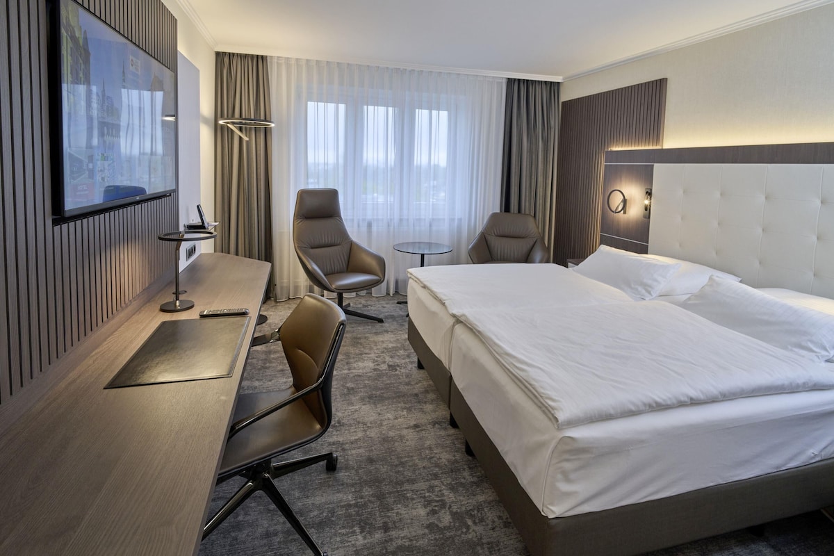 Een hotelkamer met een bed, bureau, twee stoelen, een tafeltje en een aan de muur bevestigde televisie.